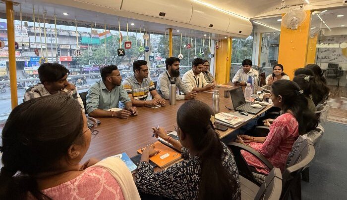 Digital marketing strategy session Amravati, Team meeting at Niksh Digital Training Institute featuring staff gathered around a large conference table. The room has a modern design with glass windows displaying digital marketing logos and symbols. Laptops, notebooks, and water bottles are placed on the table, indicating a productive discussion and collaborative learning environment. The atmosphere reflects enthusiasm and teamwork.